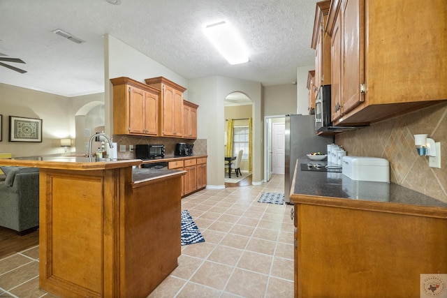 kitchen featuring tasteful backsplash, a textured ceiling, kitchen peninsula, and light tile patterned flooring