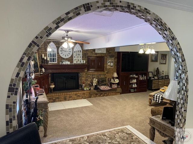 living room with brick wall, ceiling fan with notable chandelier, ornamental molding, carpet, and a brick fireplace