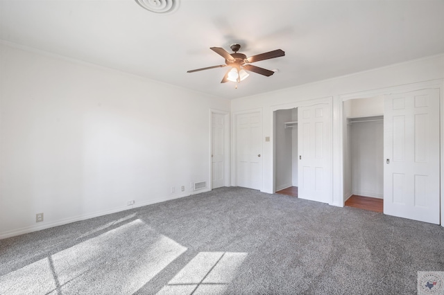 unfurnished bedroom with dark colored carpet, two closets, and ceiling fan