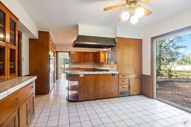 kitchen featuring wall chimney exhaust hood, tile countertops, light tile patterned floors, and a wealth of natural light