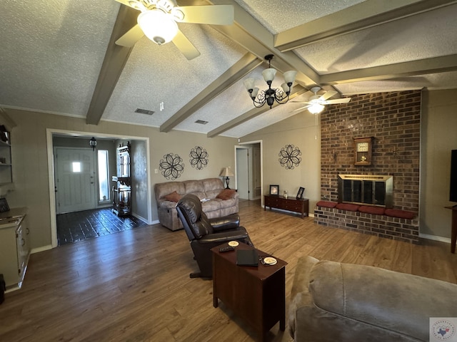 living area with a textured ceiling, lofted ceiling with beams, ceiling fan with notable chandelier, wood finished floors, and a brick fireplace