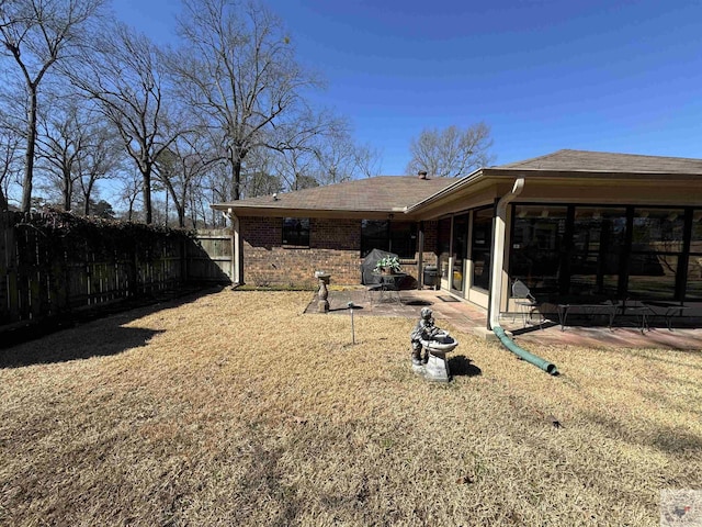 exterior space featuring roof with shingles, brick siding, a lawn, a patio area, and fence