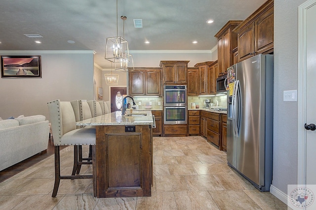 kitchen featuring appliances with stainless steel finishes, decorative light fixtures, backsplash, a kitchen bar, and a kitchen island with sink