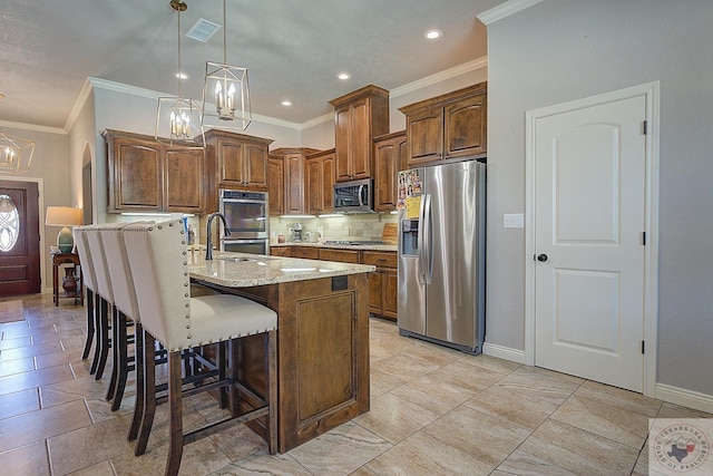 kitchen featuring decorative light fixtures, light stone counters, a kitchen island with sink, decorative backsplash, and stainless steel appliances