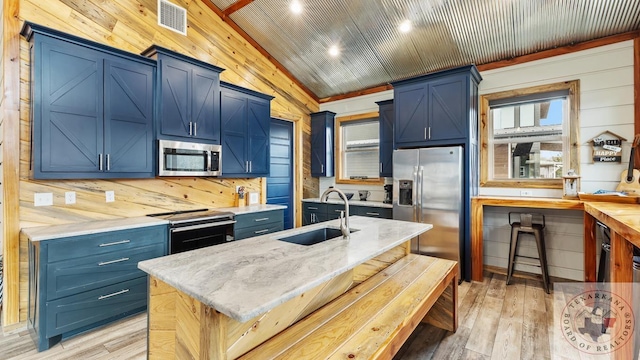 kitchen featuring a center island with sink, blue cabinetry, stainless steel appliances, lofted ceiling, and a sink