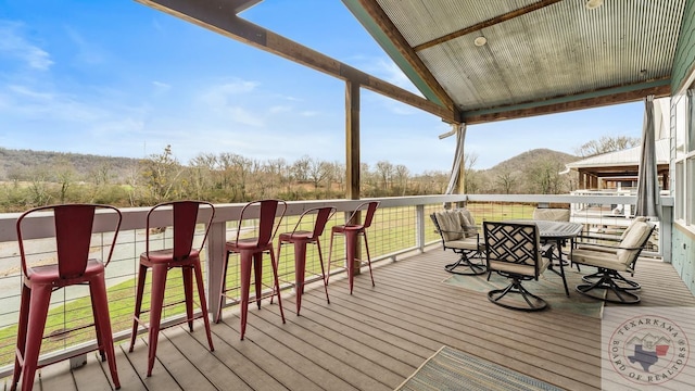 wooden terrace featuring outdoor dining space, exterior bar, and a mountain view