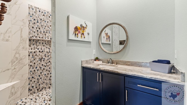 bathroom with a textured wall, a tile shower, and vanity