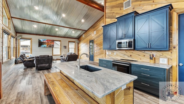 kitchen featuring an island with sink, open floor plan, stainless steel appliances, blue cabinetry, and a sink