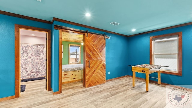 interior space with a barn door, visible vents, baseboards, ornamental molding, and light wood-style floors