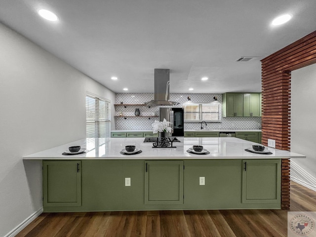 kitchen with a wealth of natural light, backsplash, island range hood, green cabinetry, and stainless steel refrigerator