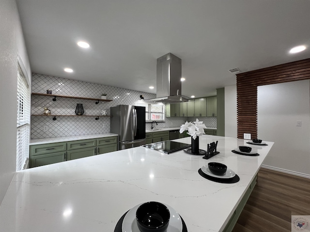 kitchen with decorative backsplash, island range hood, green cabinetry, and stainless steel refrigerator