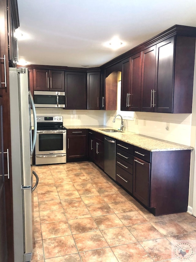 kitchen featuring sink, stainless steel appliances, light tile patterned floors, light stone countertops, and dark brown cabinetry