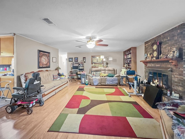 living area with visible vents, a ceiling fan, a brick fireplace, a textured ceiling, and wood finished floors