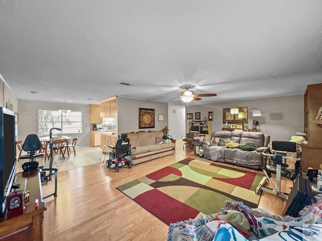 living room with ceiling fan with notable chandelier, visible vents, a textured ceiling, and light wood-style flooring