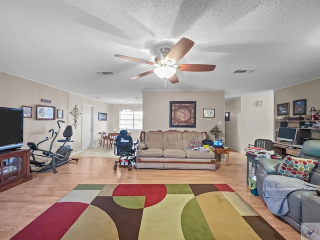 living area with ceiling fan, a textured ceiling, visible vents, and wood finished floors