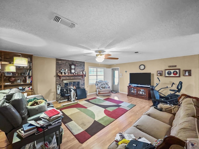 living area featuring a textured ceiling, ceiling fan, a fireplace, wood finished floors, and visible vents