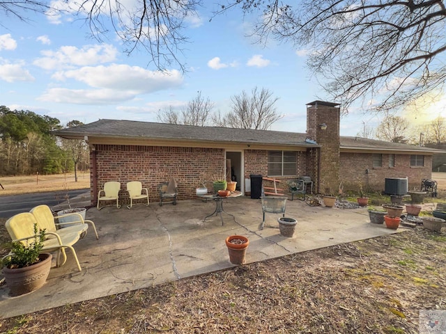 rear view of property with a patio area, a chimney, central AC unit, and brick siding