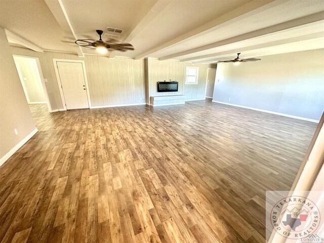 unfurnished living room featuring a large fireplace, ceiling fan, beamed ceiling, and hardwood / wood-style floors