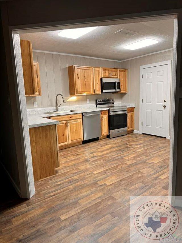 kitchen featuring crown molding, wood-type flooring, sink, a textured ceiling, and stainless steel appliances