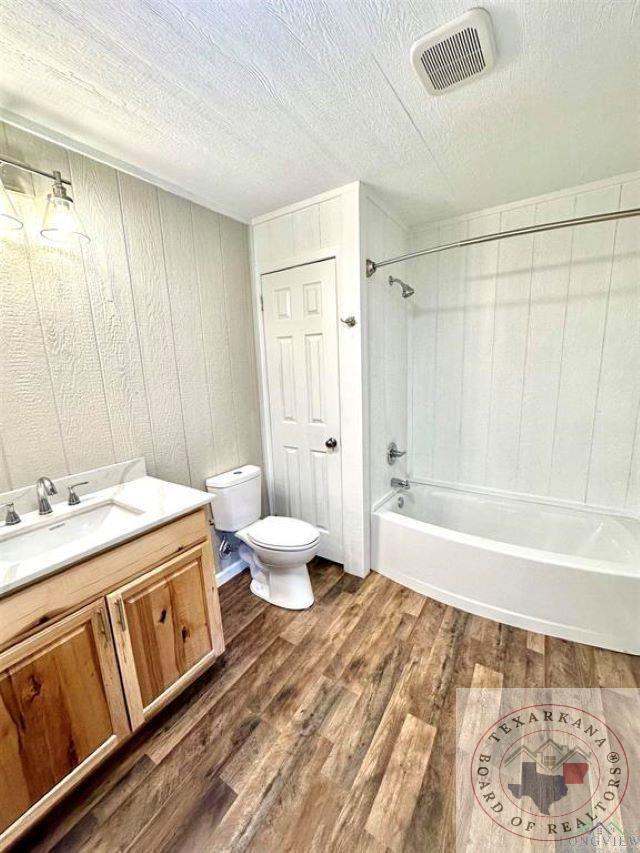 full bathroom featuring toilet, a textured ceiling, hardwood / wood-style flooring, vanity, and tiled shower / bath