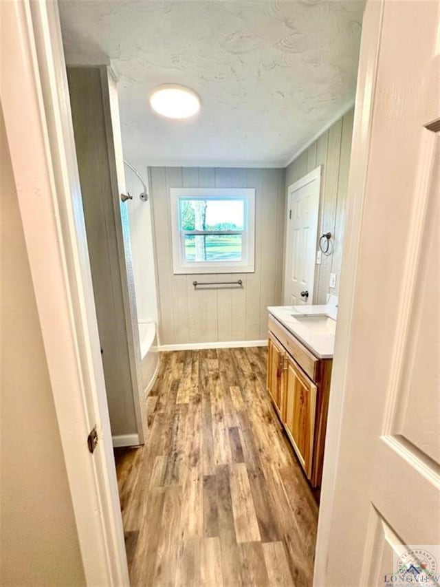 bathroom with tub / shower combination, hardwood / wood-style floors, wooden walls, and vanity