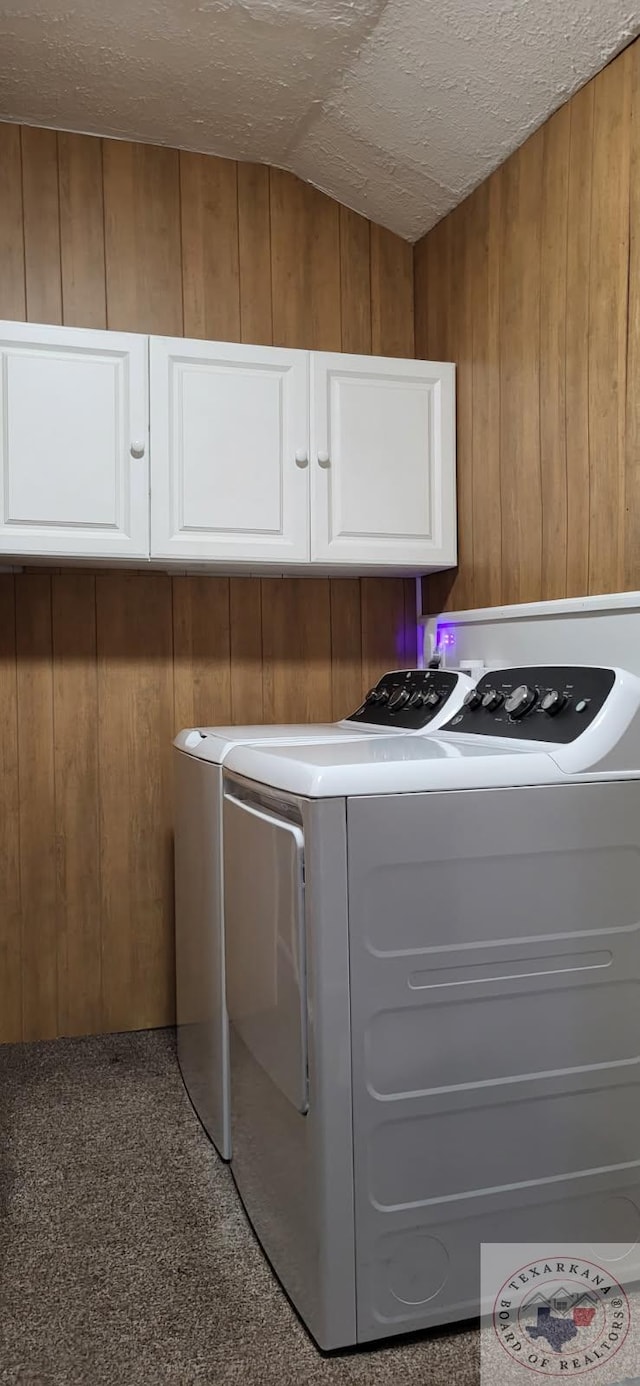 washroom featuring washing machine and dryer, cabinets, a textured ceiling, and wood walls