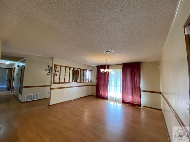 spare room with a textured ceiling, hardwood / wood-style floors, and a notable chandelier