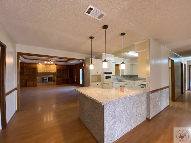 kitchen with white appliances, a brick fireplace, decorative light fixtures, kitchen peninsula, and dark hardwood / wood-style flooring