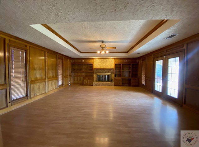 unfurnished living room featuring ceiling fan, a brick fireplace, a raised ceiling, and wood-type flooring