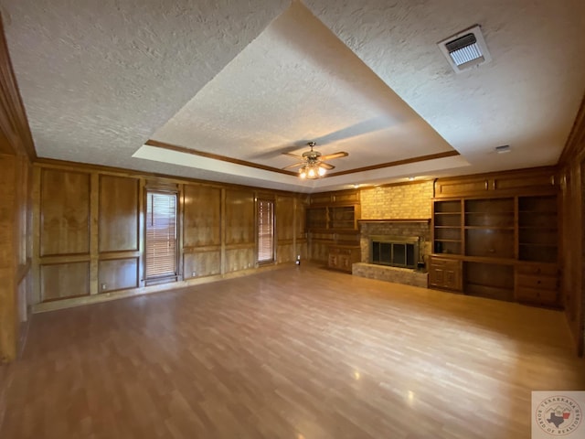 unfurnished living room with ceiling fan, hardwood / wood-style flooring, a raised ceiling, and a fireplace