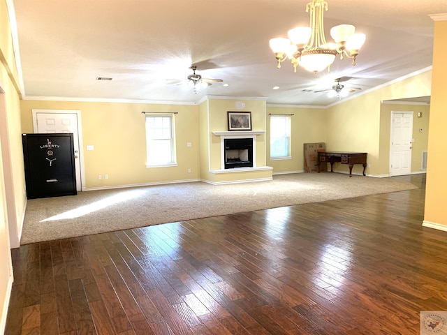 unfurnished living room featuring a wealth of natural light, a fireplace with raised hearth, ceiling fan with notable chandelier, and crown molding