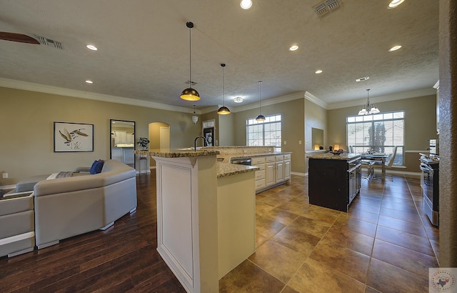 kitchen featuring crown molding, hanging light fixtures, light stone countertops, a kitchen island with sink, and a textured ceiling