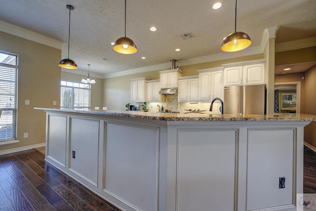 kitchen featuring white cabinets, decorative light fixtures, stainless steel refrigerator, and a spacious island