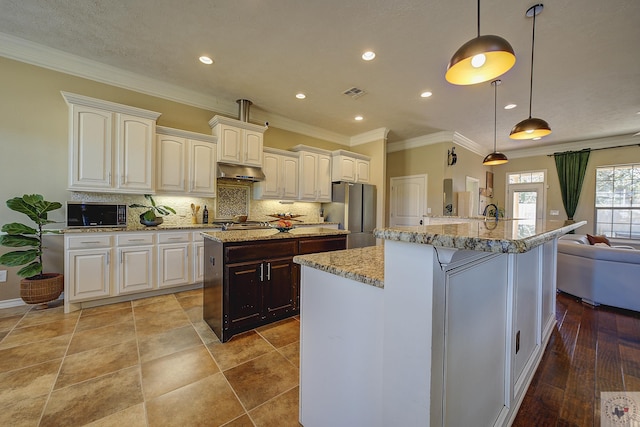 kitchen featuring hanging light fixtures, white cabinetry, light stone countertops, an island with sink, and stainless steel appliances