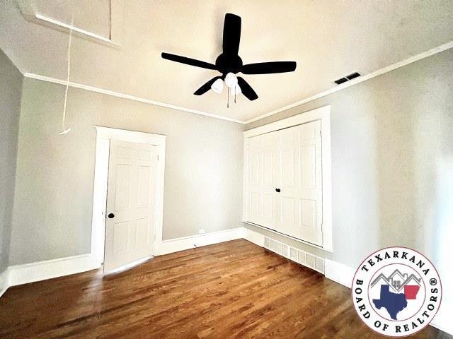 unfurnished bedroom featuring ornamental molding, visible vents, wood finished floors, attic access, and baseboards