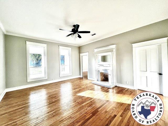 unfurnished living room featuring visible vents, baseboards, ornamental molding, a ceiling fan, and wood finished floors