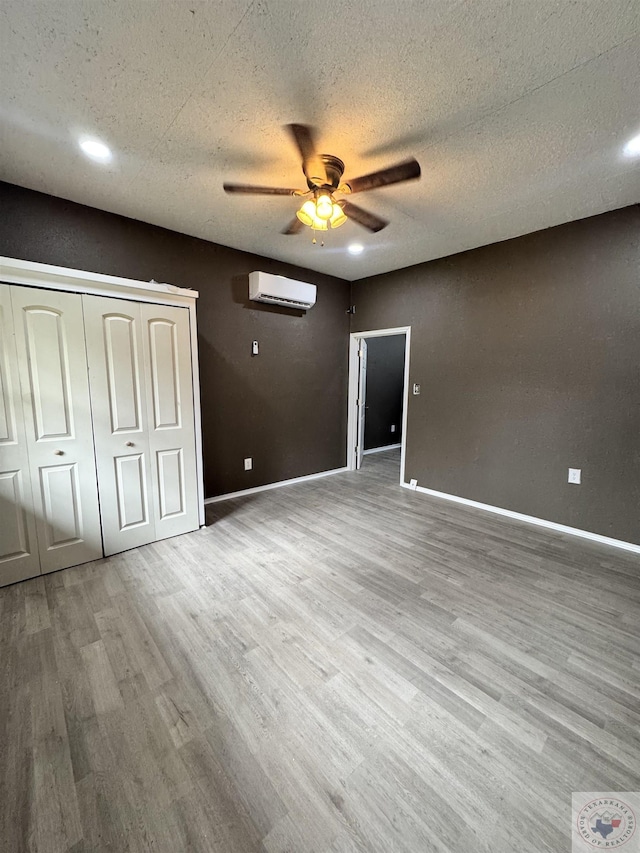 unfurnished bedroom featuring ceiling fan, a textured ceiling, light hardwood / wood-style flooring, and a wall mounted AC