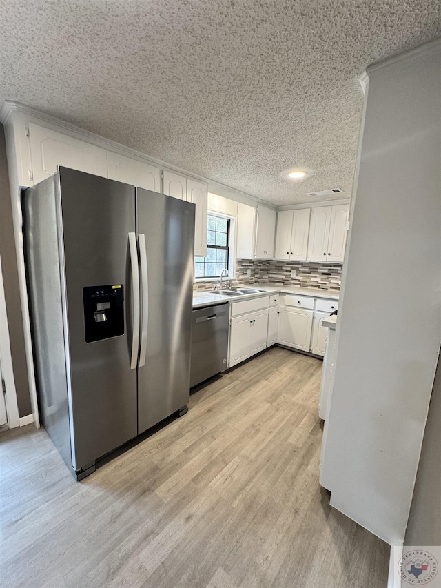 kitchen featuring sink, backsplash, white cabinets, light wood-type flooring, and stainless steel appliances