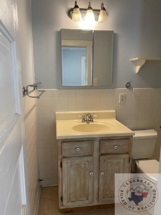 bathroom with toilet, vanity, tile patterned floors, and tile walls