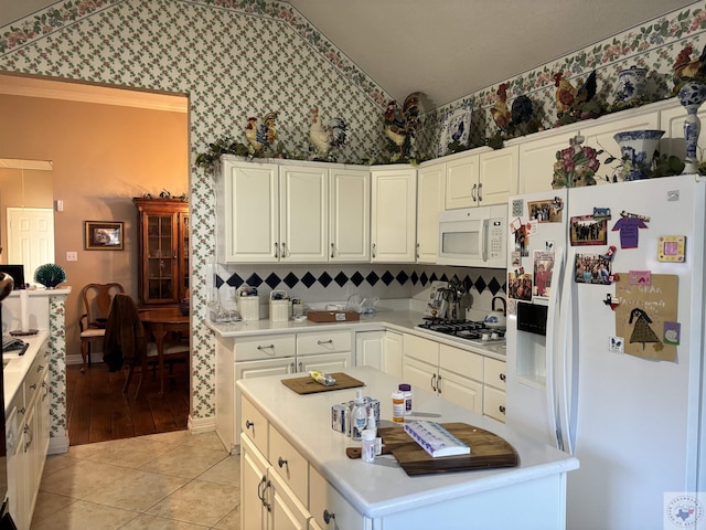 kitchen with white appliances, vaulted ceiling, white cabinets, backsplash, and light tile patterned flooring