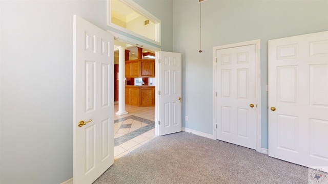 unfurnished bedroom with light carpet, a towering ceiling, and ornate columns