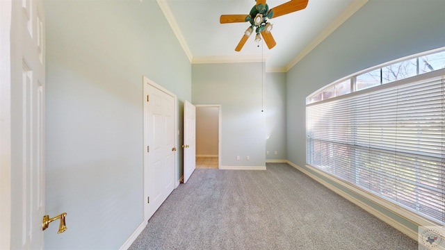 carpeted spare room featuring crown molding, a towering ceiling, and ceiling fan