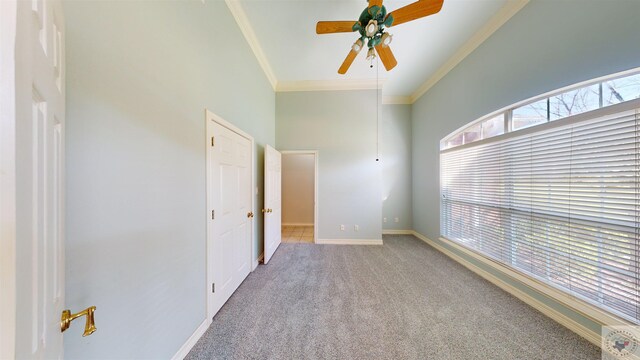 carpeted spare room featuring crown molding, a towering ceiling, and ceiling fan