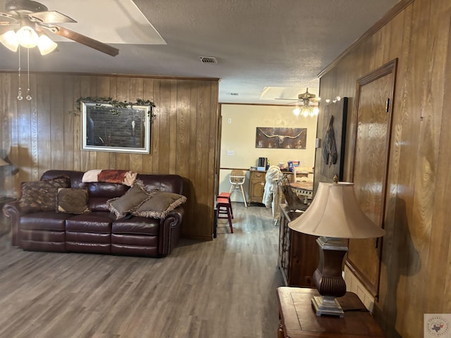 living room with hardwood / wood-style flooring, a textured ceiling, ceiling fan, and wood walls