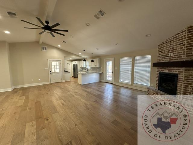 33 Timberlane St, Texarkana, TX 75501 - unfurnished living room featuring ceiling fan, a brick fireplace, visible vents, and vaulted ceiling with beams