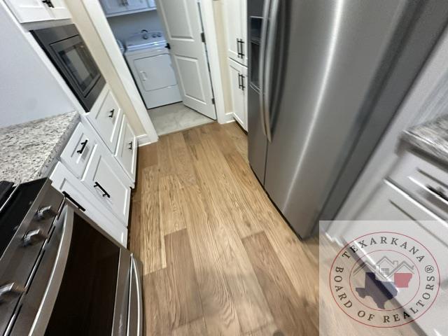 33 Timberlane St, Texarkana, TX 75501 - kitchen with washer / dryer, light wood-style flooring, white cabinetry, stainless steel fridge, and light stone countertops