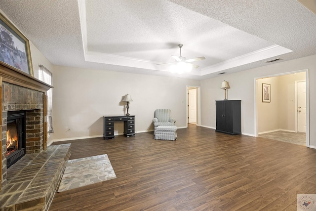 unfurnished room with a brick fireplace, a textured ceiling, a tray ceiling, and dark hardwood / wood-style floors