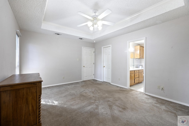 unfurnished bedroom with light carpet, ceiling fan, ensuite bathroom, a raised ceiling, and a textured ceiling