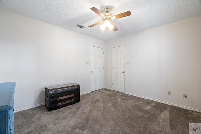 empty room featuring ceiling fan, dark carpet, and a textured ceiling