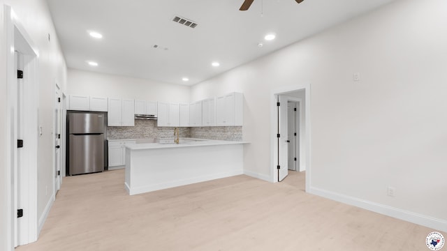 kitchen with a peninsula, light wood finished floors, visible vents, and freestanding refrigerator
